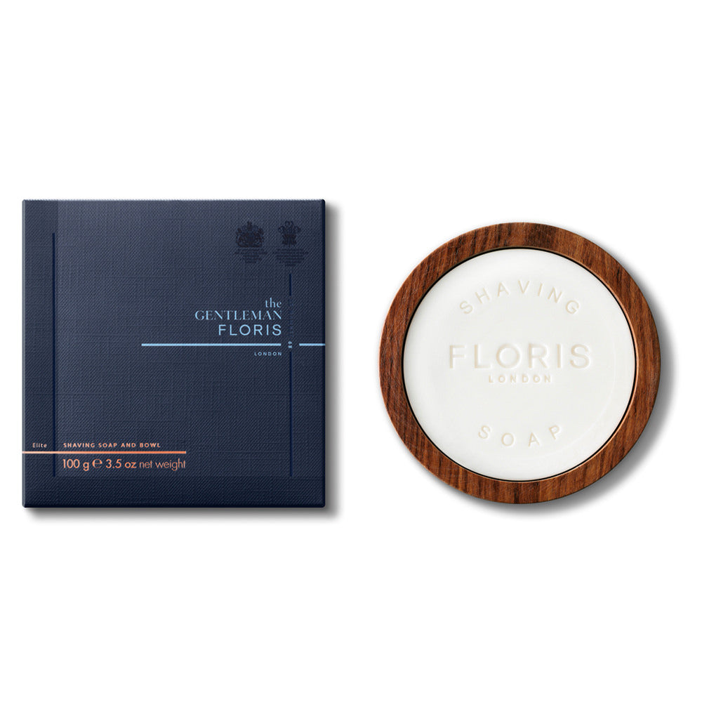 Die exklusive Floris London Elite Rasierseife in einer hochwertigen Holzschale, 100g, wird neben ihrer ansprechenden dunkelblauen Verpackung präsentiert. Dieses Set vereint klassische Eleganz mit zeitgemäßem Design und bietet somit ein erstklassiges Rasiererlebnis.