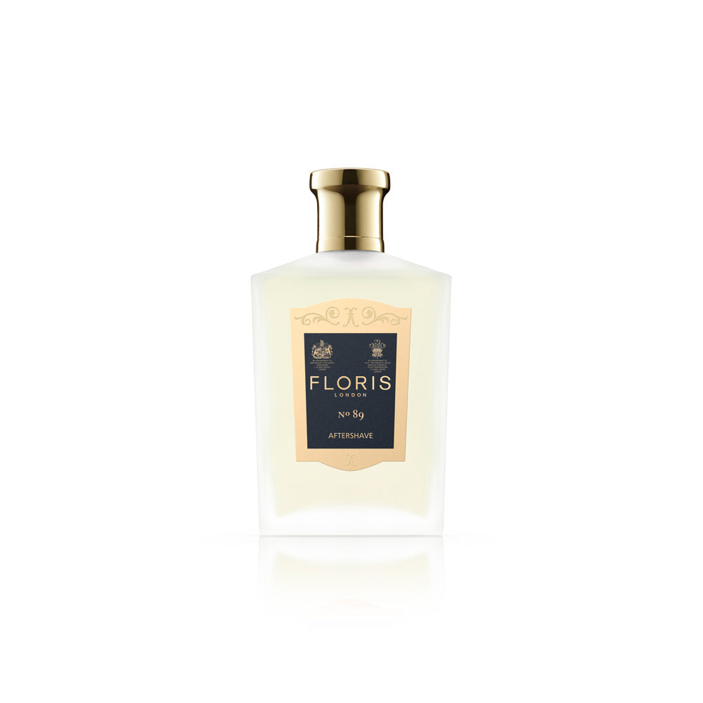 Das exklusive Aftershave-Flakon von Floris London No 89 besticht durch sein elegantes Design. Der goldfarbene Verschluss und die klare Flüssigkeit verleihen dem Produkt eine luxuriöse Note. Das Etikett ist minimalistisch gestaltet und strahlt gleichzeitig königlichen Charme aus. Es ist in einem dominanten Cremeton gehalten und mit traditionellen königlichen Wappen verziert. Die schwarze Typografie rundet das edle Erscheinungsbild ab.