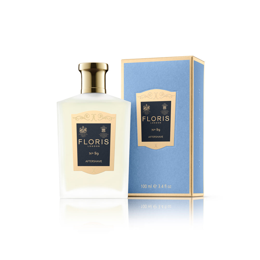 Ein Flakon des Floris London No 89 Aftershaves, mit blauer Verpackung und goldenen Details sowie dem königlichen Wappen, vermittelt ein exklusives und hochwertiges Erscheinungsbild. Das Produkt präsentiert sich in einer transparenten, flüssigen Form und wird durch eine elegante, cremefarbene Etikettierung besonders betont.